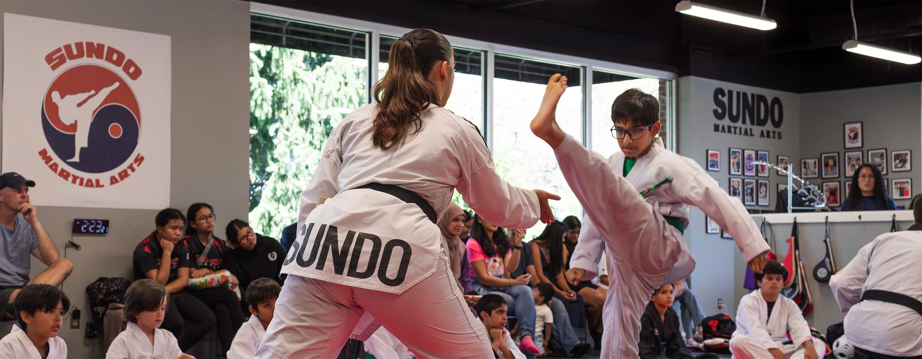 Master Jennifer Raiz holding a kicking bag for a young student during testing